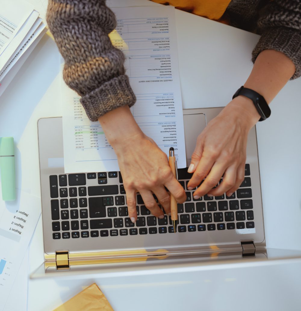 Person typing on laptop with documents nearby.