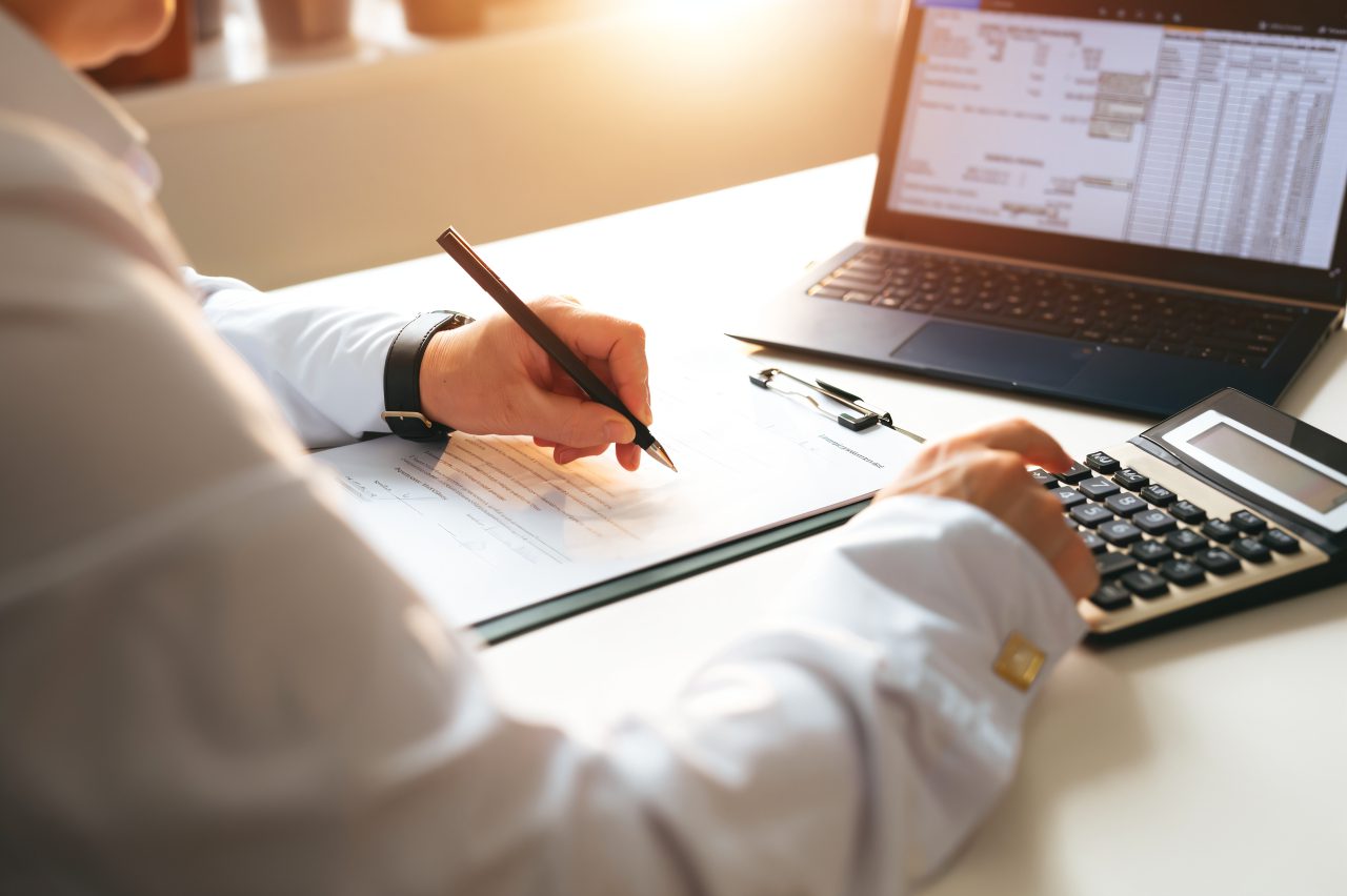 Person calculating finances with laptop and documents.