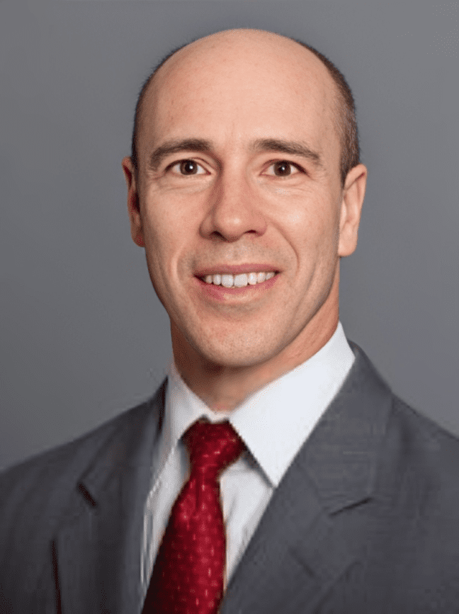 Man in suit with red tie smiling.