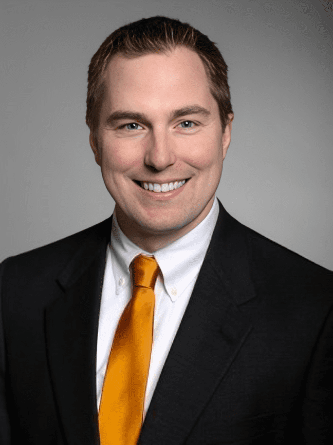 Smiling man in suit with orange tie.